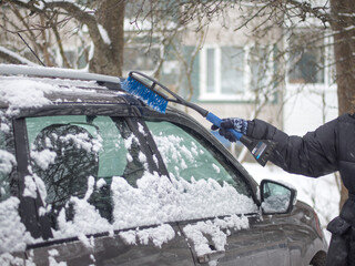 A girl cleans the car window from snow with a brush