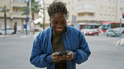 Smiling african woman with braids using a smartphone on a city street.