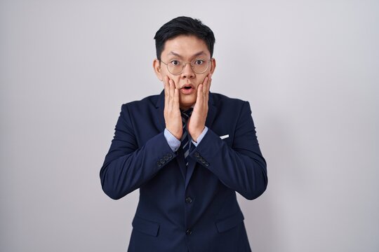 Young asian man wearing business suit and tie afraid and shocked, surprise and amazed expression with hands on face