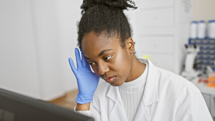African american woman scientist in lab wearing gloves analyzing data on computer screen
