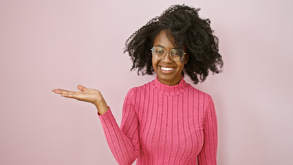 Smiling african american woman presenting in a pink sweater against a plain background indoors.