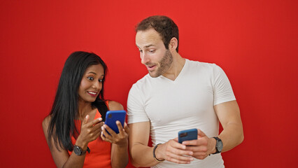 Beautiful couple using smartphones smiling over isolated red background