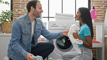 Beautiful couple smiling confident washing clothes at laundry room