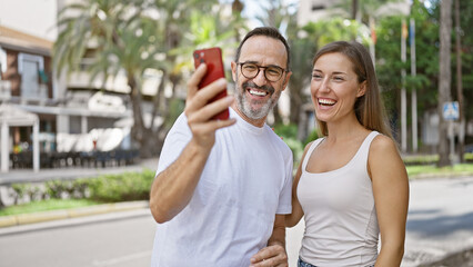 Obraz premium Confident father and daughter share a lovely moment, joyfully taking a cool selfie on their mobile phone standing on a bustling city street.