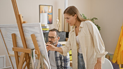 In an art studio, two focused artists - a man and woman, intently draw on canvas, deepening their...