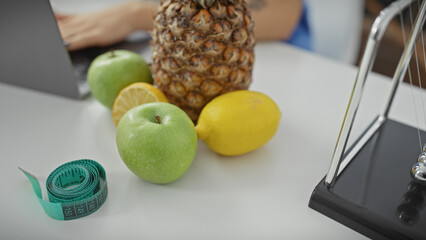 A woman's partial portrait in a clinic with laptop, fruits, and measuring tape on the desk indicates healthcare and diet.