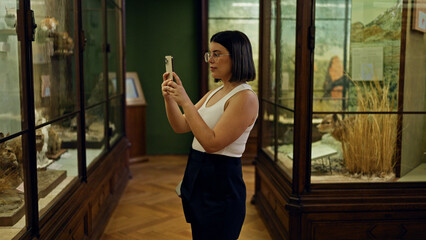 Young beautiful hispanic woman visiting natural history exhibition taking pictures at Natural...