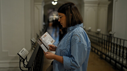 Young beautiful hispanic woman visiting crypt reading brochure at Imperial Crypt in Vienna