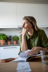Pensive serious woman sitting at table planning budget, looking at window while thinking over...