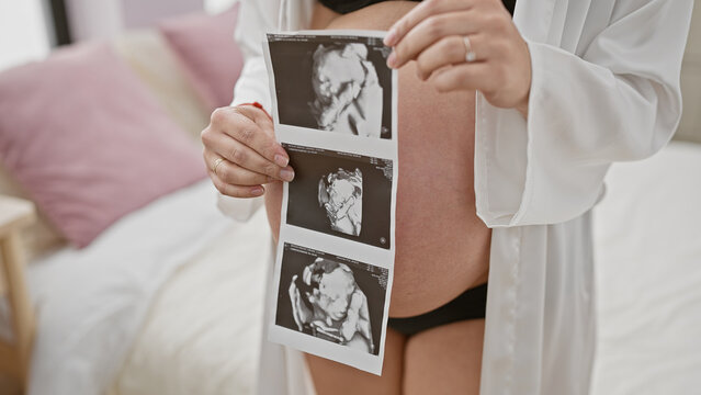 Expectant hispanic woman holding ultrasound images, standing in a bedroom, symbolizing pregnancy, maternity, and anticipation.