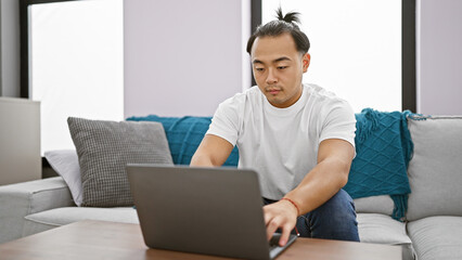 Handsome young chinese man, focused and concentrated, working online using laptop while sitting on...