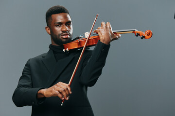 Elegant African American man playing the violin in a black suit against a gray background