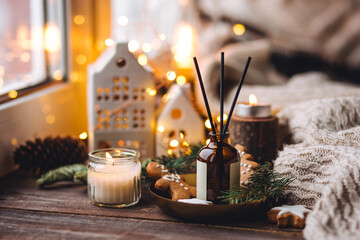 Xmas spirit, simple way to creating holiday atmosphere and festive mood at home on the window sill. Scented burning aromatic candles on wooden tray, liquid reed diffuser with sticks, fir tree branch