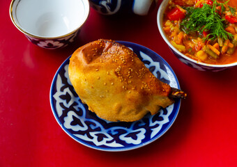 National Uzbek dish samsa with mutton served on red table in blue and white plate with portion of laghman.