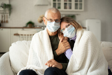 Cold winter, elderly husband and wife wearing protective face masks at home.