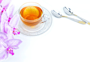 a transparent cup of aromatic tea and a pink orchid on a white background
