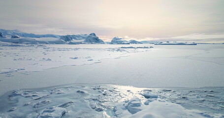 Fly over frozen Antarctic ocean sunset landscape. Snow covered untouched wilderness of South Pole. Desert white land of snow and ice aerial drone shot. Mountains in background. Nature conservation © mozgova