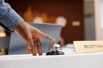 Man standing at empty reception desk, using service call bell to get attention of hotel employees,...