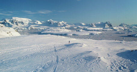 Man running Antarctica snow hill aerial view. People travel, active lifestyle, sport, recreation in Antarctic wild nature landscape. Snow covered mountains, icy ocean, sunny winter day. Drone flight © mozgova