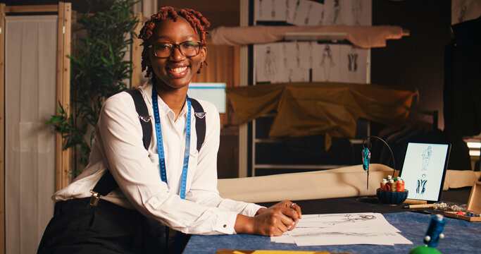Young couturier reviewing sketches on clothes in modern workshop, checking fabric design to create luxury fashion items. Female tailor working on crafting clothes in atelier, needlework.