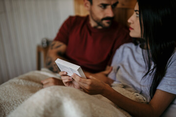 Couple finding solace in each other while reading pregnancy test guidelines in bed