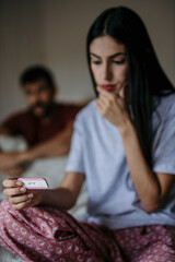 Concerned couple discussing unexpected news while holding a pregnancy test in bedroom