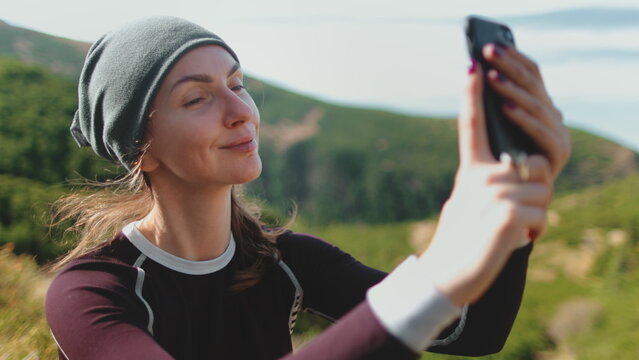 Tourist woman takes a selfie photo on smartphone in mountain nature landscape. Caucasian girl hiker enjoys beautiful views. Travel, tourism, holiday, trekking, hiking, active lifestyle