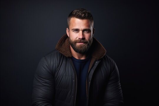 Portrait of a handsome bearded man in a black jacket on a dark background.