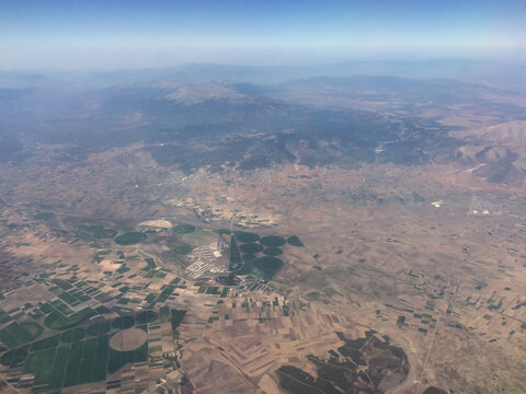 View from above of different colored fields, forests and small towns below. View from the plane