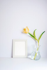 Blank picture frame and yellow tulip in vase on the white background. Holiday, Women's Day or Mother's Day concept