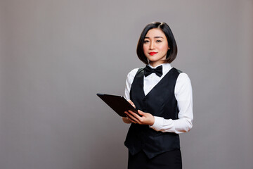 Smiling confident asian waitress wearing professional uniform, holding digital tablet and looking at camera. Young attractive hospitality industry receptionist using portable gadget portrait