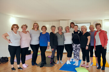 A vibrant community of senior women, guided by their instructor, embraces the enriching journey of yoga, fostering unity, well-being, and a shared commitment to active aging