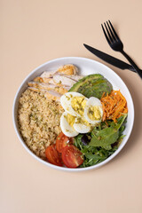 A plate with eggs, vegetables, couscous and meat on beige background top view