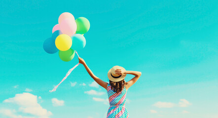 Happy joyful woman with bunch of colorful balloons in summer straw hat on blue sky background