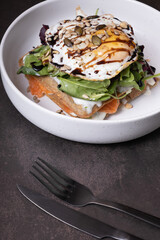 Bowl of waffles with salmon and egg with seeds on dark background angle view