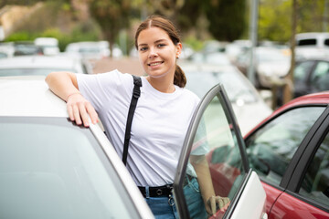 Portrait of a positive confident girl standing near an open car, about to get in it to go on the road