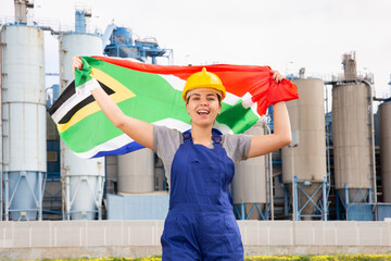Cheerful female worker in hardhat with south african flag standing in front of factory