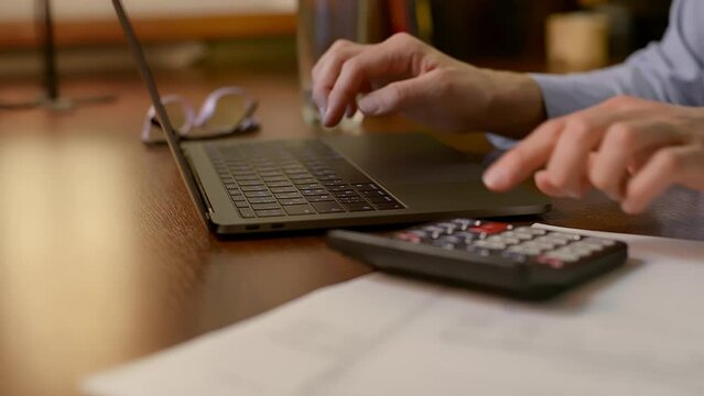 Close up view of woman hands using a calculator laptop, pay bills online. Sitting at table with receipt invoice, managing expenses, household budget, analyzing financial data, accounting, e-banking.