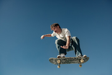 Active man doing tricks in the air on his skateboard at the skate park on blue sky background