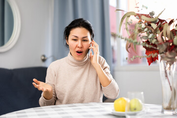 Fototapeta na wymiar Asian woman having telephone conversation while sitting at table at home.