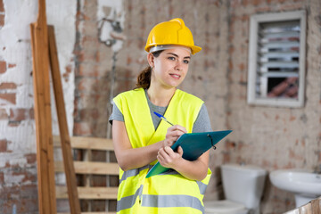 Caucasian woman engineer checking documents during repair works indoors.