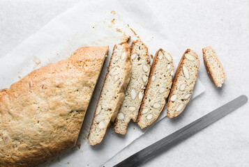 slicing almond biscotti on white parchment lined tray, almond cantucci cookies on a white chopping board, flatlay of slices of biscotti cookies or twice baked cookies