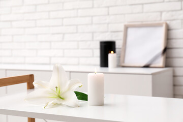 Burning candle and beautiful lily flower on light table in room