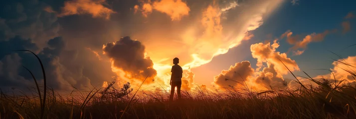 Fototapeten A figure stands in a field, gazing at a dramatic sky with rays of sunlight piercing through clouds. © Alena