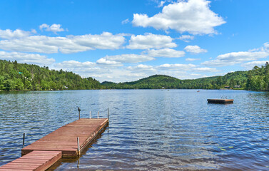 Tranquil lake reflects a vibrant blue sky dotted with fluffy clouds. Long wooden pier stretching into the calm water.