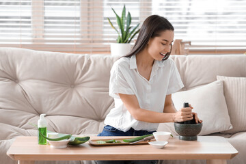 Beautiful young happy woman making organic cosmetics with aloe vera in living room