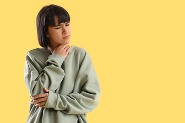 Young woman suffering from neck pain on yellow background