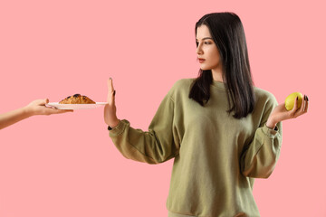 Young woman with apple rejecting croissant on pink background. Diet concept