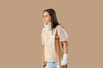 Injured young woman after accident with crutches on brown background