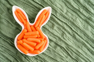 Fresh raw baby carrots in an Easter Bunny shaped white ceramic dish, health and nutrition on a...